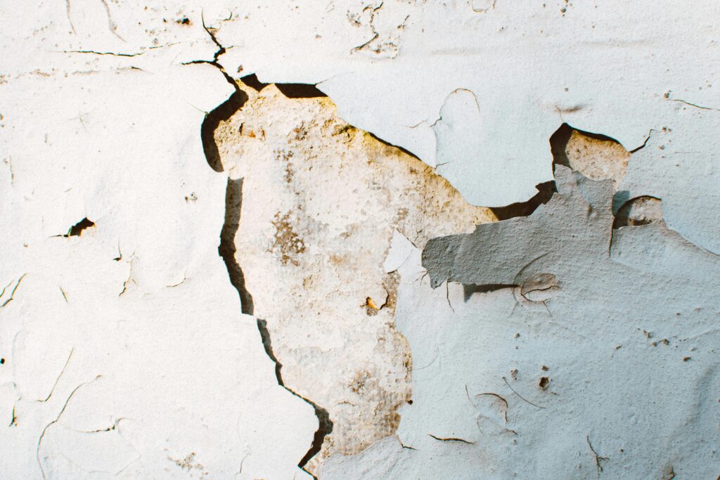 Close-up of a cracked plaster wall with peeling paint revealing decaying texture.